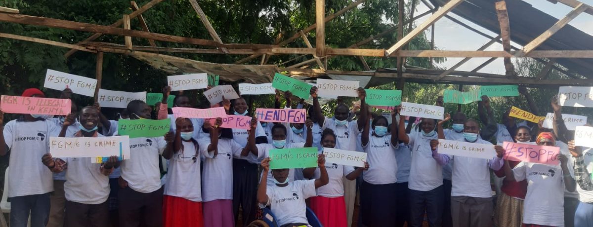 A group of people smiling holding 'End FGM/C' signs