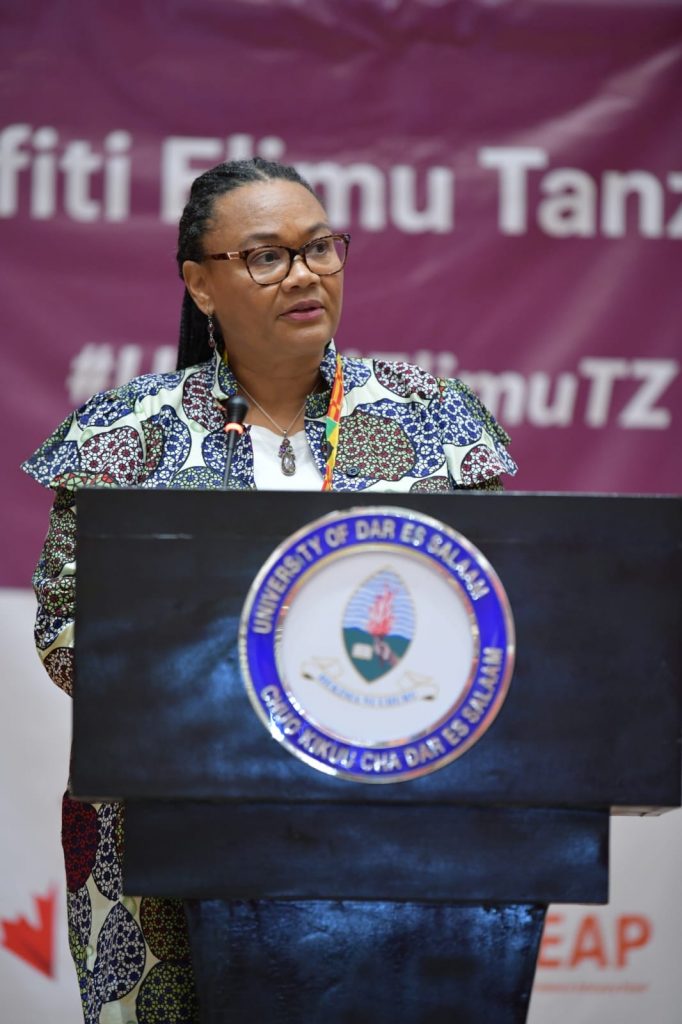 Photo of a woman stood behind a podium, speaking into a microphone, wearing a colourful outfit 